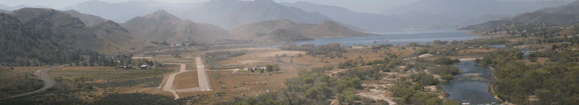 A panoramic view of a mountainous landscape with a small airport, lake, and river.