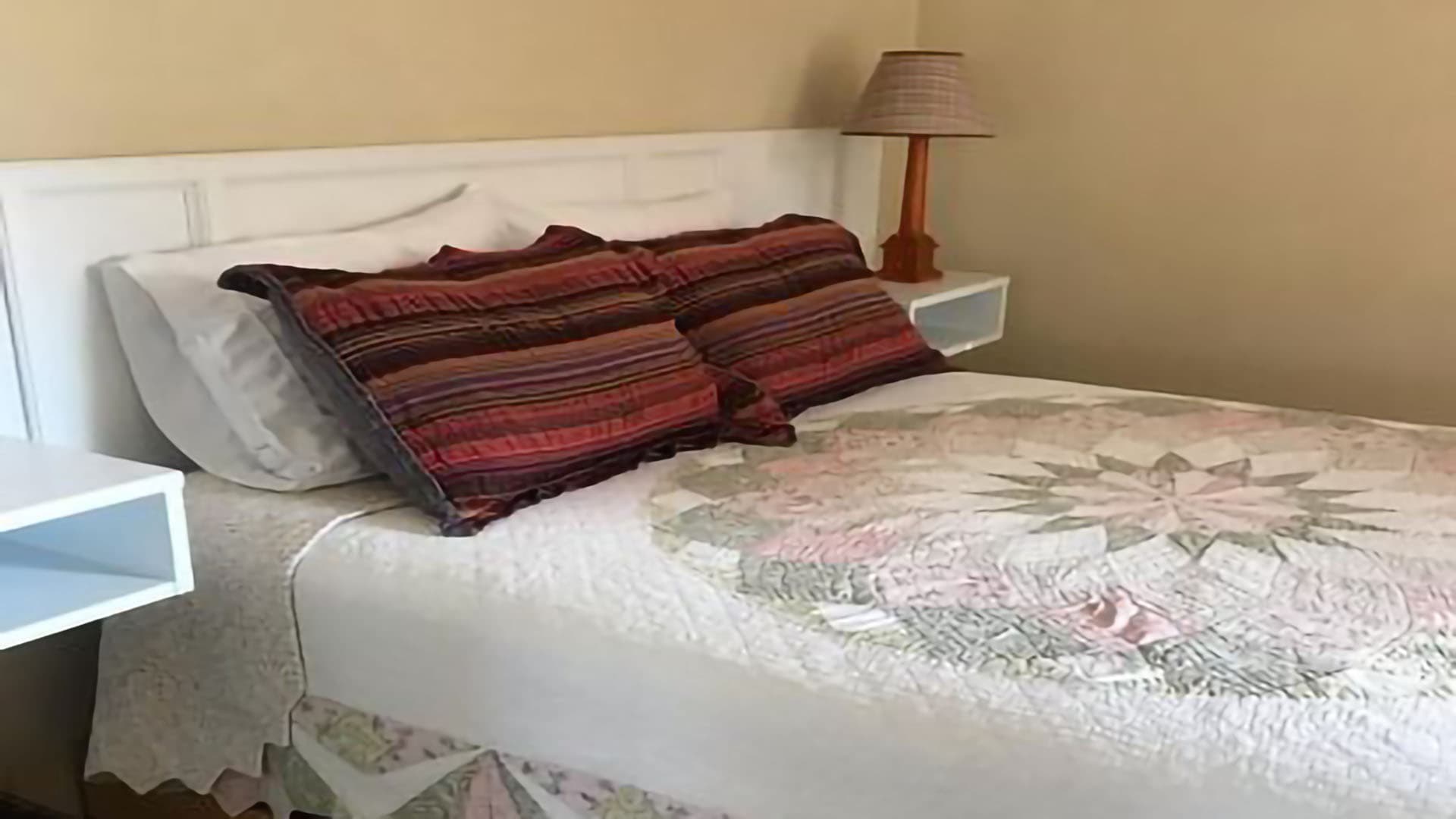 A neatly made bed with a patterned quilt and colorful pillows in a cozy room.