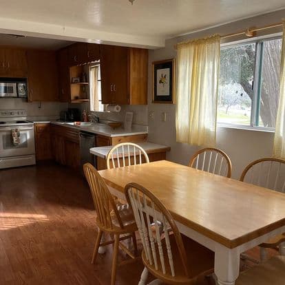A cozy kitchen featuring wooden cabinets, a dining table, and bright natural light from a window.