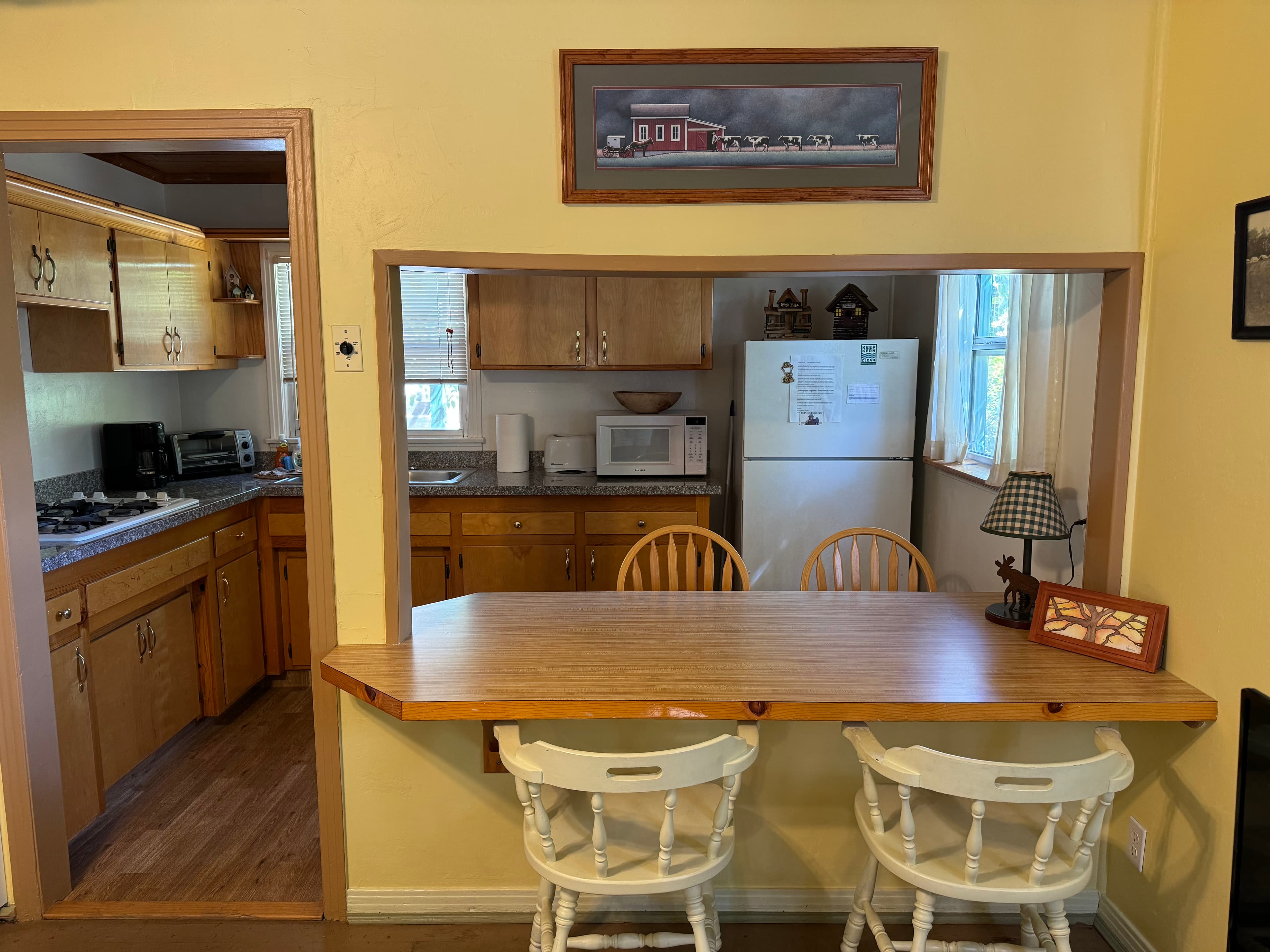 A view of a cozy kitchen with wooden cabinets, a breakfast bar, and a small dining area.