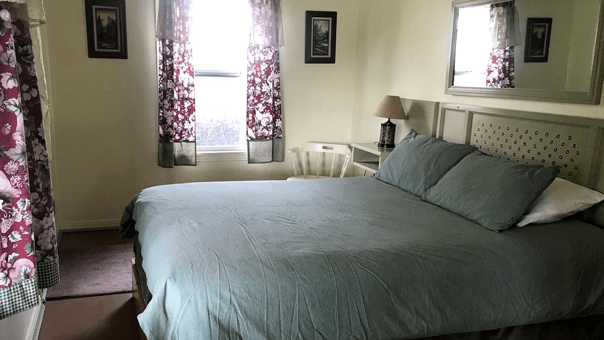 A cozy bedroom featuring a large bed, floral curtains, and a small bedside table.