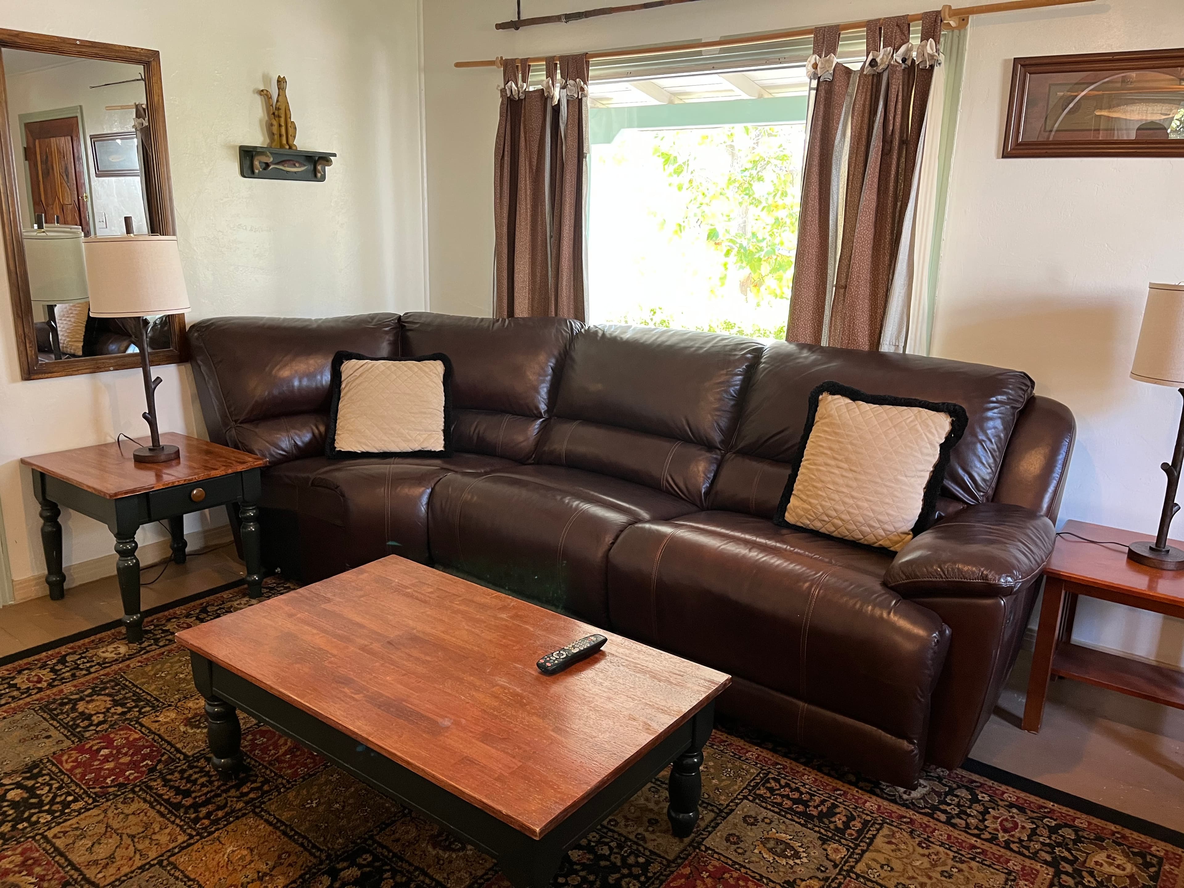 A brown leather sofa with throw pillows sits in a cozy living room alongside a wooden coffee table and lamps.