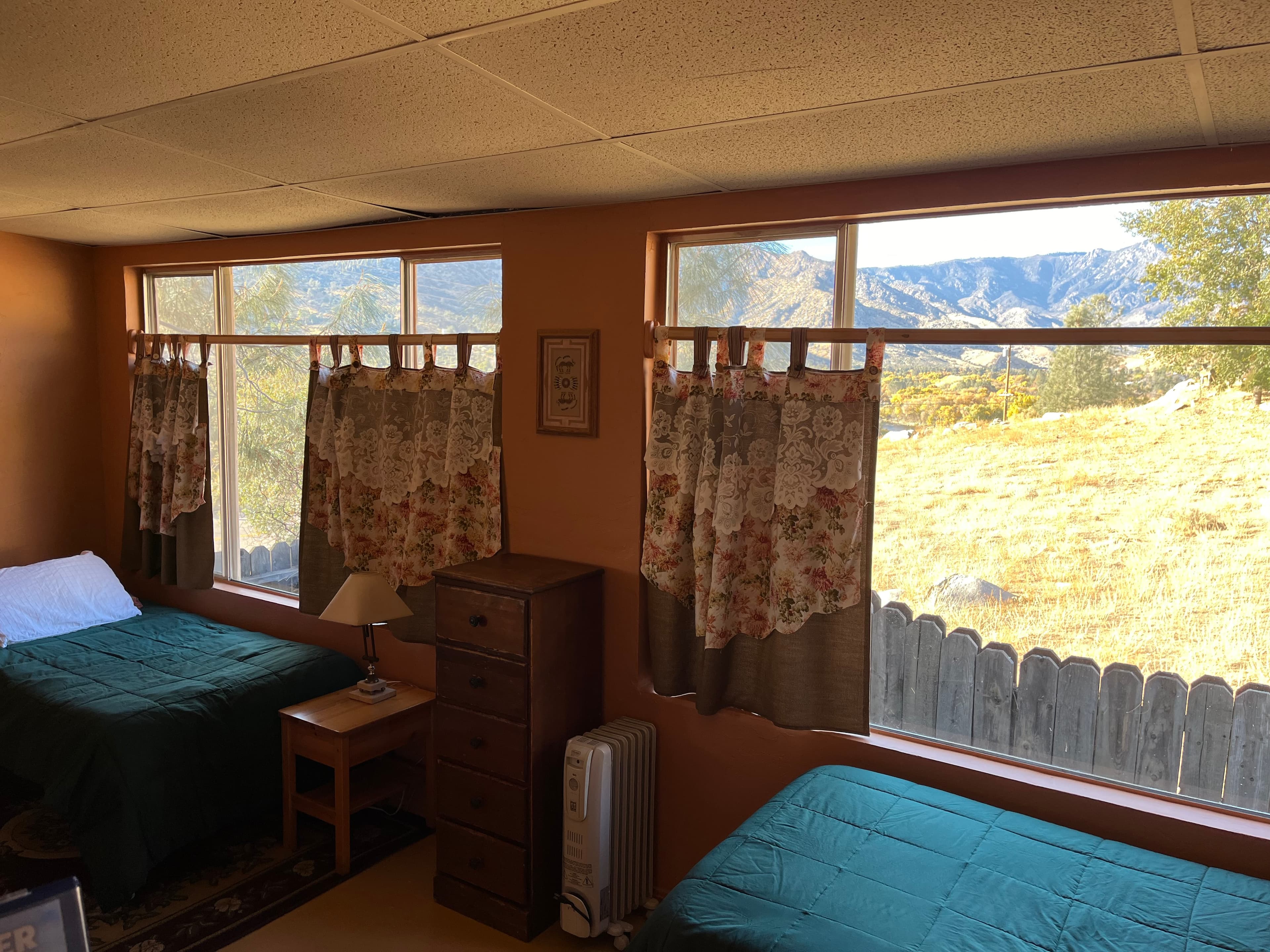 A cozy bedroom with two beds, a nightstand, and large windows showcasing a mountain view.