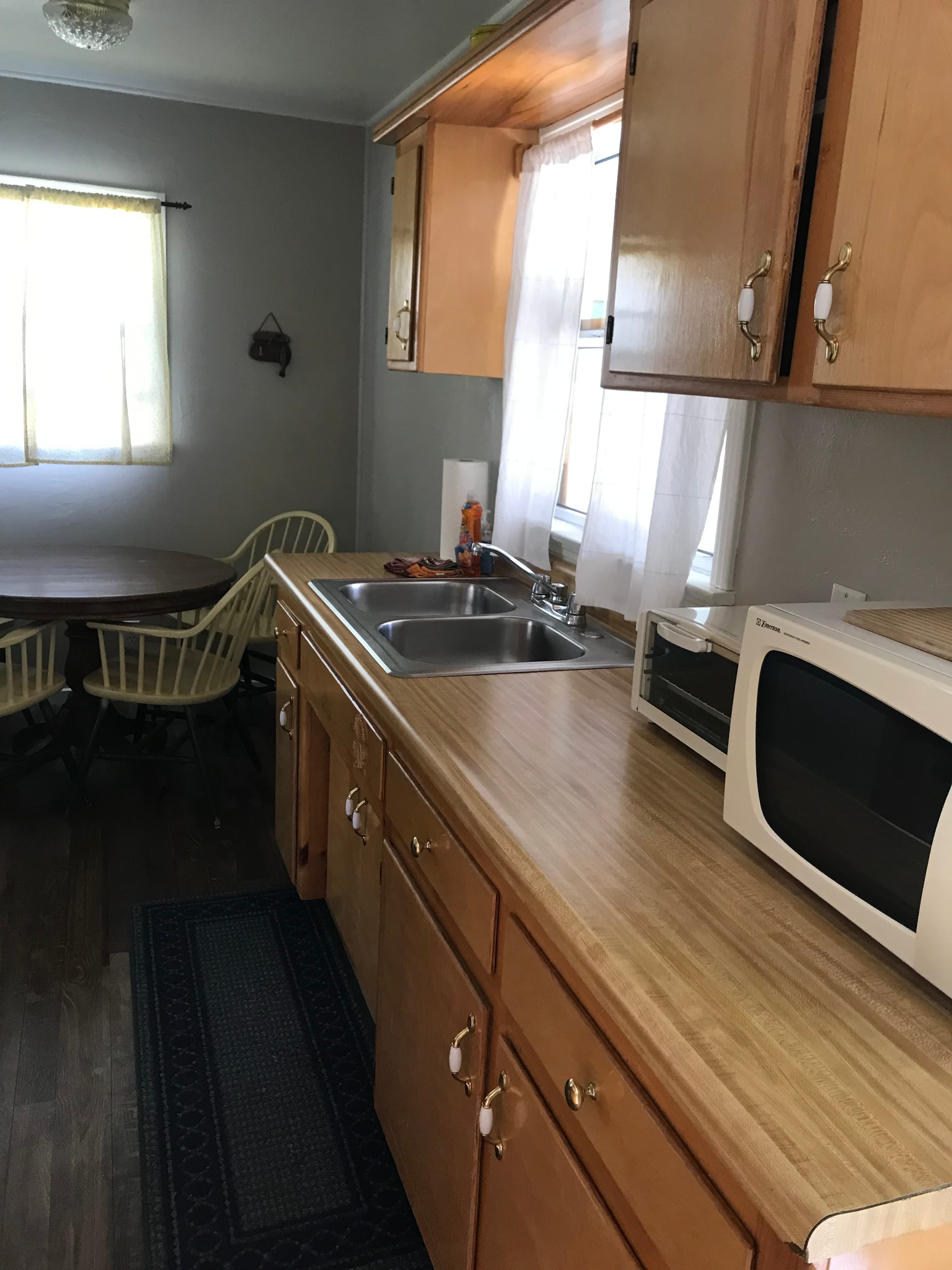 A bright kitchen with wooden cabinets, a sink, a microwave, and a dining table with yellow chairs.