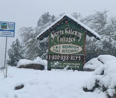 A snow-covered sign for Sierra Gateway Cottages displaying rental information and contact details.