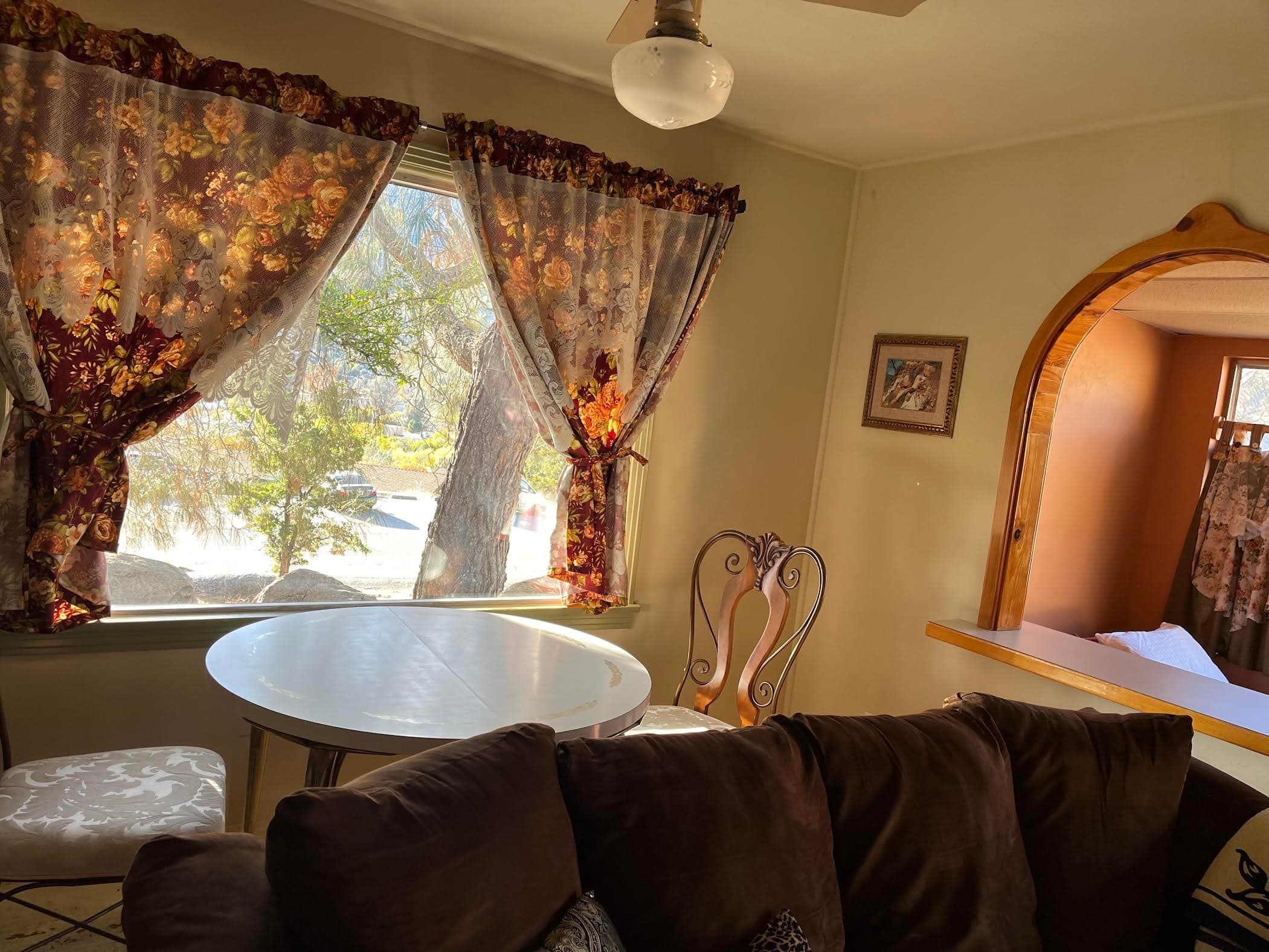 A cozy living space featuring a round table, floral curtains, and a brown couch.