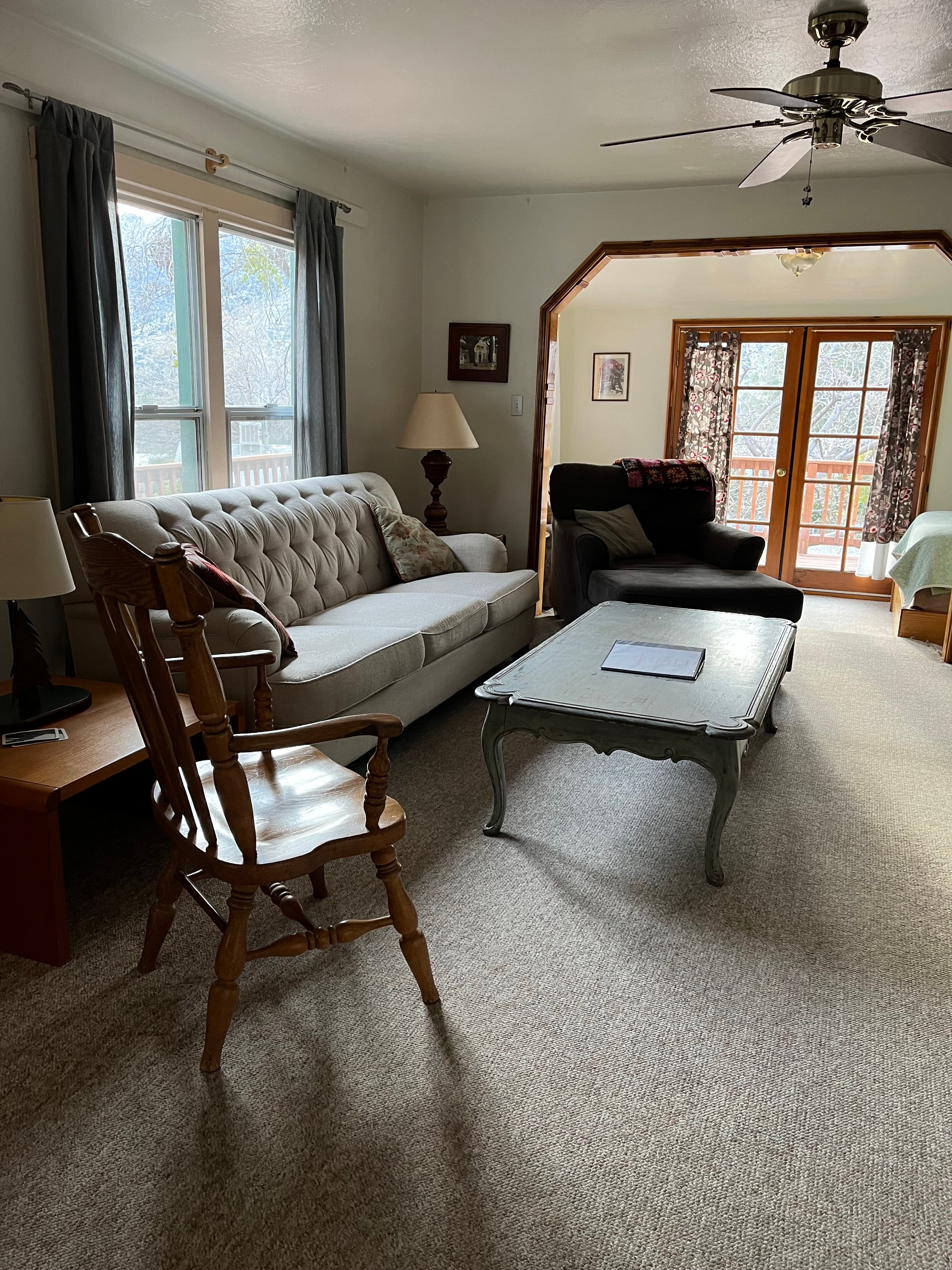 A cozy living room with a sofa, rocking chair, coffee table, and large windows overlooking a deck.